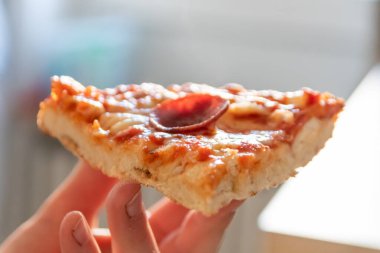 Çocuk eli sıcak buharlı ve lezzetli peynirli pizza salamını tutuyor. Makro görüntüdeki İtalyan lezzetini diyet fast food yemekleri için kalorili sağlıksız bir aperatif olarak görüyor.