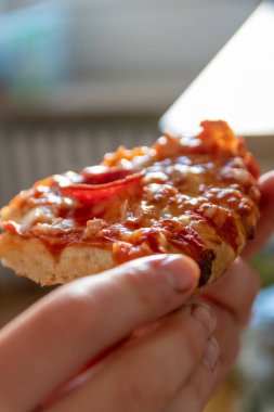 Çocuk eli sıcak buharlı ve lezzetli peynirli pizza salamını tutuyor. Makro görüntüdeki İtalyan lezzetini diyet fast food yemekleri için kalorili sağlıksız bir aperatif olarak görüyor.