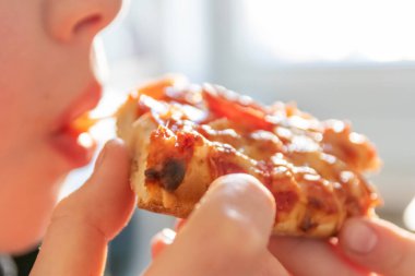 Çocuk eli sıcak buharlı ve lezzetli peynirli pizza salamını tutuyor. Makro görüntüdeki İtalyan lezzetini diyet fast food yemekleri için kalorili sağlıksız bir aperatif olarak görüyor.