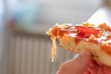Çocuk eli sıcak buharlı ve lezzetli peynirli pizza salamını tutuyor. Makro görüntüdeki İtalyan lezzetini diyet fast food yemekleri için kalorili sağlıksız bir aperatif olarak görüyor.