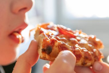 Çocuk eli sıcak buharlı ve lezzetli peynirli pizza salamını tutuyor. Makro görüntüdeki İtalyan lezzetini diyet fast food yemekleri için kalorili sağlıksız bir aperatif olarak görüyor.