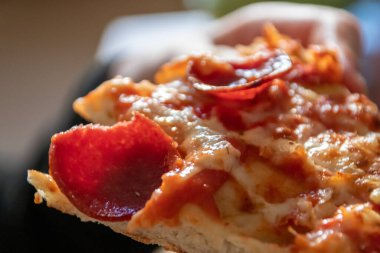 Çocuk eli sıcak buharlı ve lezzetli peynirli pizza salamını tutuyor. Makro görüntüdeki İtalyan lezzetini diyet fast food yemekleri için kalorili sağlıksız bir aperatif olarak görüyor.
