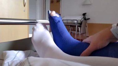 Aşil tendonu olan Avrupalı bir adam hastane yatağında özel ayakkabı ve koltuk değnekleri ile yatıyor.