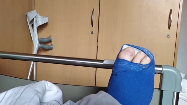 欧洲男性阿基里斯肌腱断裂患者经手术后躺在医院病床上 有特殊的鞋子和拐杖用于急诊后的康复治疗 — 图库视频影像