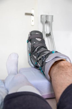 Achilles tendon yırtılması ameliyatından sonra Avrupalı bir adam özel fizyoterapi ayakkabısı ve iyileşmek için koltuk değnekleriyle eve döndü.