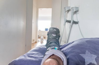 Achilles tendon yırtılması ameliyatından sonra Avrupalı bir adam özel fizyoterapi ayakkabısı ve iyileşmek için koltuk değnekleriyle eve döndü.