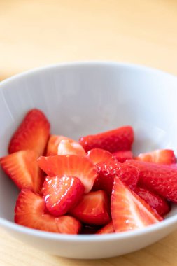 Kâsede kesilen çileklerin çoğu gümüş kaşıkla ya da lezzetli parmak yemekleriyle ve sağlıklı atıştırmalıklarla yenilebilir besin ve sağlık için ahşap mutfak masasında kırmızı meyve ve vitaminlerle yemeye hazırdır.