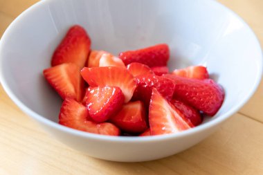 Kâsede kesilen çileklerin çoğu gümüş kaşıkla ya da lezzetli parmak yemekleriyle ve sağlıklı atıştırmalıklarla yenilebilir besin ve sağlık için ahşap mutfak masasında kırmızı meyve ve vitaminlerle yemeye hazırdır.