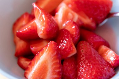 Kâsede kesilen çileklerin çoğu gümüş kaşıkla ya da lezzetli parmak yemekleriyle ve sağlıklı atıştırmalıklarla yenilebilir besin ve sağlık için ahşap mutfak masasında kırmızı meyve ve vitaminlerle yemeye hazırdır.