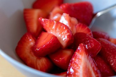 Kâsede kesilen çileklerin çoğu gümüş kaşıkla ya da lezzetli parmak yemekleriyle ve sağlıklı atıştırmalıklarla yenilebilir besin ve sağlık için ahşap mutfak masasında kırmızı meyve ve vitaminlerle yemeye hazırdır.