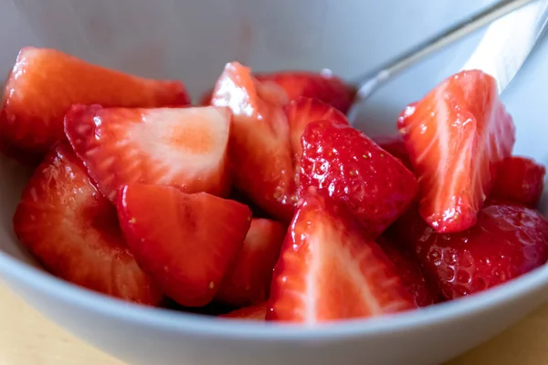 Kâsede kesilen çileklerin çoğu gümüş kaşıkla ya da lezzetli parmak yemekleriyle ve sağlıklı atıştırmalıklarla yenilebilir besin ve sağlık için ahşap mutfak masasında kırmızı meyve ve vitaminlerle yemeye hazırdır.