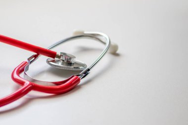 Profesyonel kardiyo kontrolü için doktorların muayenehanesinde kırmızı stetoskop ve beyaz masadaki klinik tedavi odasında kardiyoloğun kalp atışı nabız kontrolü vücut parantezlerini ölçmek için tıbbi ekipman olarak kullanılması.