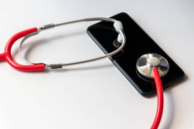 Siyah akıllı telefondaki kırmızı steteskop, dijital doktorlar için mobil cihazları olan sağlık kayıtları ve dijital hasta kayıtlarını ve modern ekipman ve teknolojiyle dijital tanı tedavisini temsil ediyor.