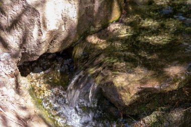 Işıl ışıl suda kayalar, berrak bir su deresinin suyunda yansıyan güneşli yansımalarla doğal arka planda zen meditasyonu, küçük dalgalar ve sağlıklı bir dağdaki ipeksi dalgalar görülüyor.