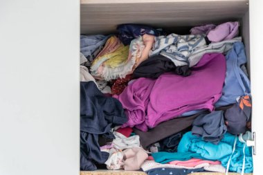 Chaotic wardrobe and sloppy closet shows many outfits of a woman with shopping addiction and many clothes like pullovers, shirts and trousers as crumpled laundry stored into a messy heap of fashion
