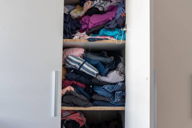 Chaotic wardrobe and sloppy closet shows many outfits of a woman with shopping addiction and many clothes like pullovers, shirts and trousers as crumpled laundry stored into a messy heap of fashion