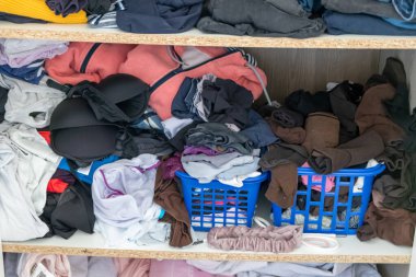 Chaotic wardrobe and sloppy closet shows many outfits of a woman with shopping addiction and many clothes like pullovers, shirts and trousers as crumpled laundry stored into a messy heap of fashion