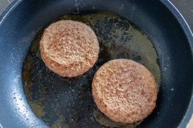 Two burger patties burger meat sizzling in hot pan with fat and oil as delicious selfmade hamburger bbq meatballs as unhealthy fast food lunch with lots of calories and cholesterol in frying pan