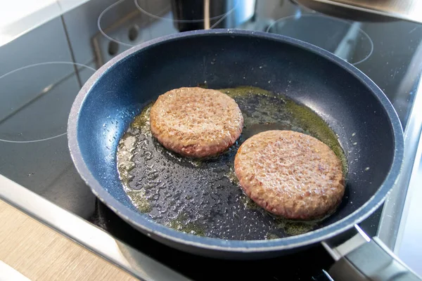 Two burger patties burger meat sizzling in hot pan with fat and oil as delicious selfmade hamburger bbq meatballs as unhealthy fast food lunch with lots of calories and cholesterol in frying pan