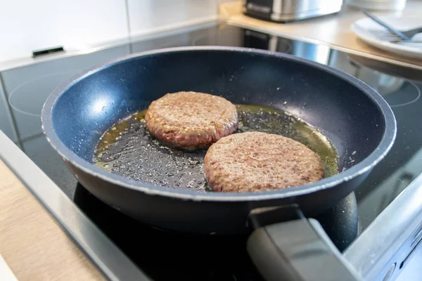 Two burger patties burger meat sizzling in hot pan with fat and oil as delicious selfmade hamburger bbq meatballs as unhealthy fast food lunch with lots of calories and cholesterol in frying pan