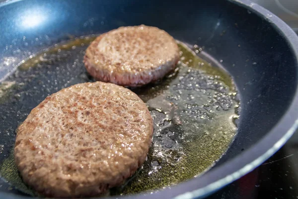 Two burger patties burger meat sizzling in hot pan with fat and oil as delicious selfmade hamburger bbq meatballs as unhealthy fast food lunch with lots of calories and cholesterol in frying pan