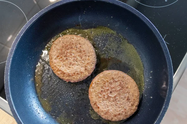 Two burger patties burger meat sizzling in hot pan with fat and oil as delicious selfmade hamburger bbq meatballs as unhealthy fast food lunch with lots of calories and cholesterol in frying pan