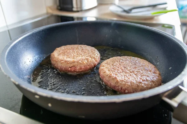 Two burger patties burger meat sizzling in hot pan with fat and oil as delicious selfmade hamburger bbq meatballs as unhealthy fast food lunch with lots of calories and cholesterol in frying pan