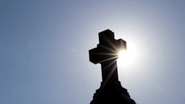 Shiny holy cross with sparkling sunbeams through foliage and sky shine a light of spiritual faith and christianity with symbol for religious death and gods resurrection in sunset cemetery grave stone