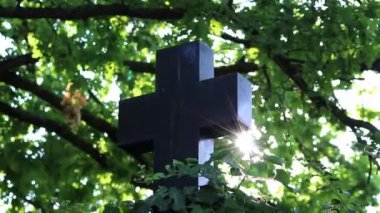 Shiny holy cross with sparkling sunbeams through foliage and sky shine a light of spiritual faith and christianity with symbol for religious death and gods resurrection in sunset cemetery grave stone