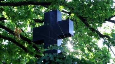 Shiny holy cross with sparkling sunbeams through foliage and sky shine a light of spiritual faith and christianity with symbol for religious death and gods resurrection in sunset cemetery grave stone