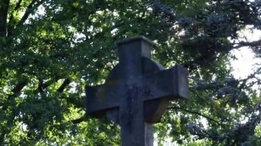 Shiny holy cross with sparkling sunbeams through foliage and sky shine a light of spiritual faith and christianity with symbol for religious death and gods resurrection in sunset cemetery grave stone