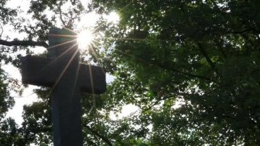 Shiny holy cross with sparkling sunbeams through foliage and sky shine a light of spiritual faith and christianity with symbol for religious death and gods resurrection in sunset cemetery grave stone