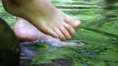 Barefooted boy cooling his feet in water with crystal clear water and idyllic floating creek in summertime shows outdoor hiking tour with little break in calm brook with the family outdoor adventures