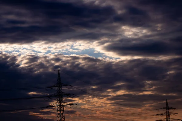 Golden sky with sun rays and lens flare shows solar energy with electricity tower pylon silhouette in golden sunset and orange sky for sustainable energy or renewable resources from dusk till dawn sun