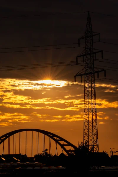 Golden sky with sun rays and lens flare shows solar energy with electricity tower pylon silhouette in golden sunset and orange sky for sustainable energy or renewable resources from dusk till dawn sun