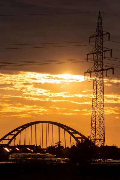 Golden sky with sun rays and lens flare shows solar energy with electricity tower pylon silhouette in golden sunset and orange sky for sustainable energy or renewable resources from dusk till dawn sun