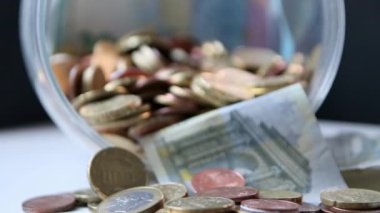 Euro money savings sliding inside glass jar full of Euro coins and Euro banknotes for financial management of pocket money and tip or gratuity for piggy bank currency pile as cash close-up macro view