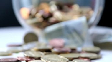 Euro money savings sliding inside glass jar full of Euro coins and Euro banknotes for financial management of pocket money and tip or gratuity for piggy bank currency pile as cash close-up macro view