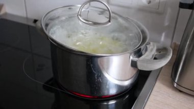 Sıcak suda patates haşlamak seramik ocakta gümüş kapta kaynatmak evde otantik yemek pişirmek ocakta patates pişirmek buhar ve baloncuklar yakın planda kapaktan çıkıyor.