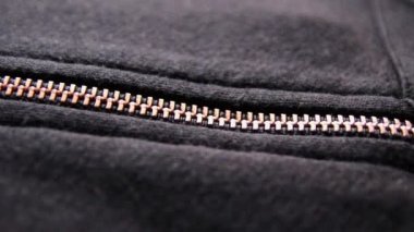 Kapalı makro görünümlü bakır renkli fermuar kısmi açık metal fermuarlı, metalik optik siyah kumaşlı siyah fermuarlı, zarif giyimli ya da stil katkı malzemeli siyah kazağı gösteriyor.