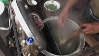 Bir adam haşlanan erişteleri karıştırıyor.