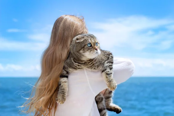 Vacation with an animal. A cat in the arms of a girl against the backdrop of the sea and sky.