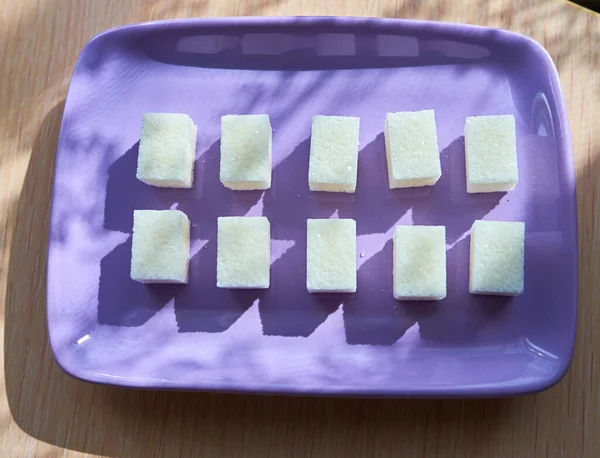 Фиолетовая тарелка с десятью кубиками белого сахара стоит на столе под солнцем. — стоковое фото