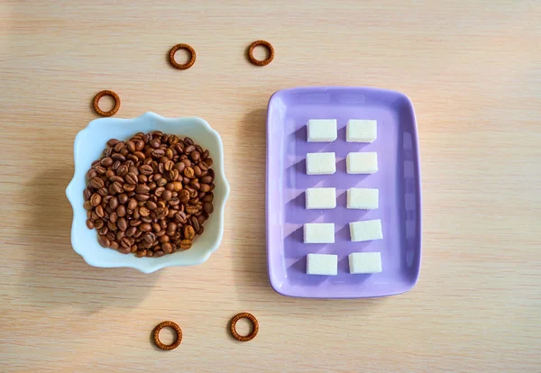 Um prato roxo com dez pedaços de açúcar branco e um prato branco com um monte de grãos de café estão sobre a mesa. Vista superior — Fotografia de Stock