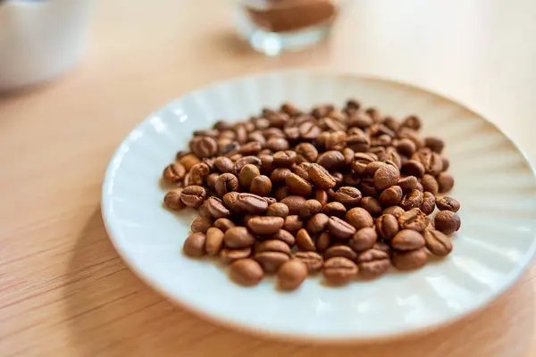 Um prato branco redondo com um punhado de grãos de café está de pé sobre a mesa. Foco seletivo — Fotografia de Stock