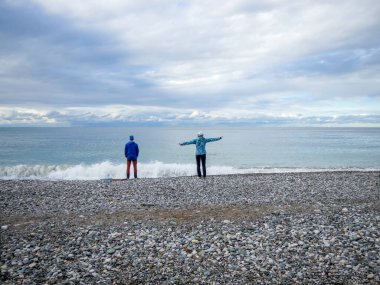 Bir adam ve bir kadın sahilde durup denizi izliyorlar.