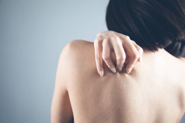 Kadın gri arka planda kendine sarılıyor.