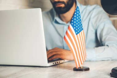 Bilgisayarda çalışan ve masasında Amerikan bayrağı olan bir adam.