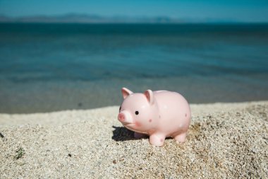 Kumsaldaki kumlu kumsalda su arka planı olan bir kumbara.