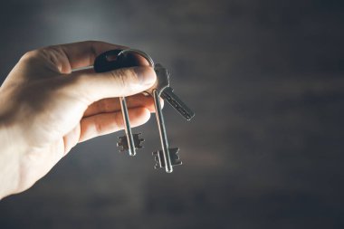 Adam evin anahtarlarını koyu arkaplanda tutuyor.